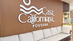 A modern outdoor seating area with a wooden slatted wall and a sign reading 'Casa Califomana Pousada'. - Pousada Casa Californiana (Garopaba)