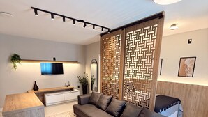 A modern living room with a sectional sofa, a wooden coffee table, a TV mounted on the wall, and a decorative partition. - Pousada Casa Californiana (Garopaba)