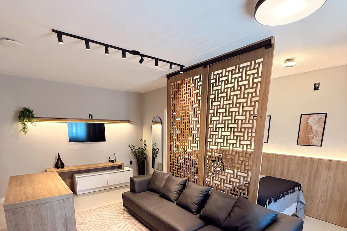 A modern living room with a sectional sofa, a wooden coffee table, a TV mounted on the wall, and a decorative partition.