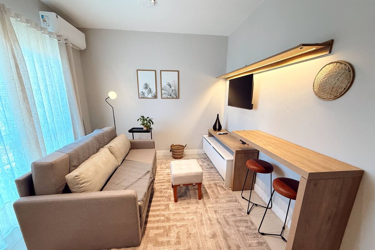 A modern living room with a sofa, a coffee table, a TV, and a small kitchen area.