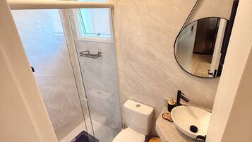 Un baño con ducha, inodoro, lavamanos y espejo.