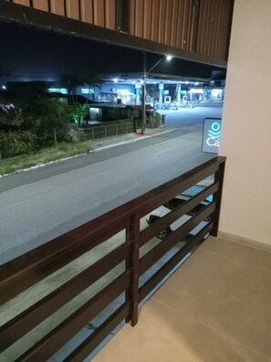 A balcony with a view of a street at night, including a gas station and a pedestrian crossing. - Pousada Casa Californiana (Garopaba)