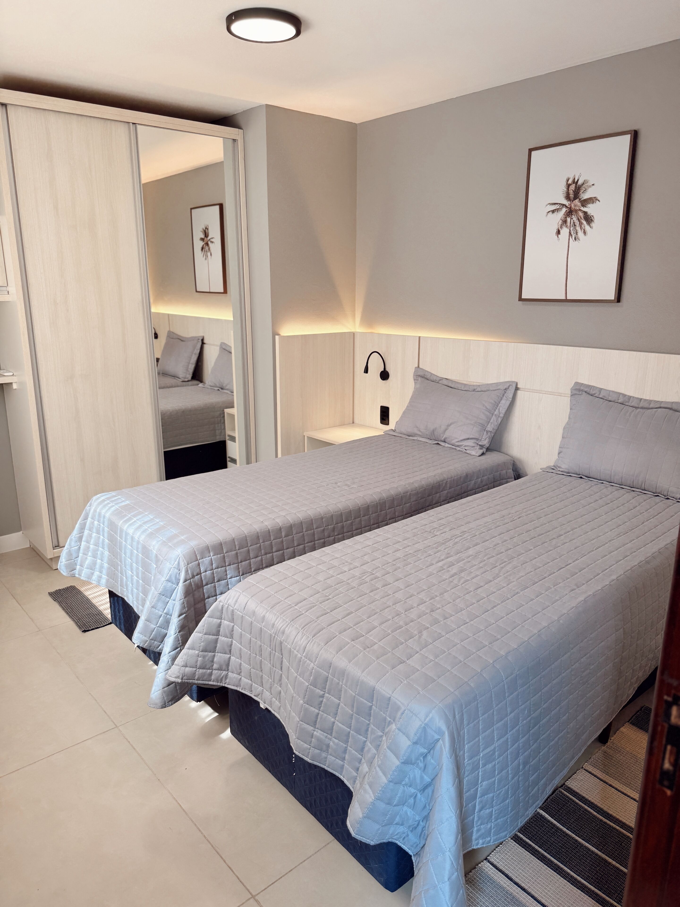 A bedroom with two beds, a nightstand, a wall-mounted lamp, and a door leading to another room.