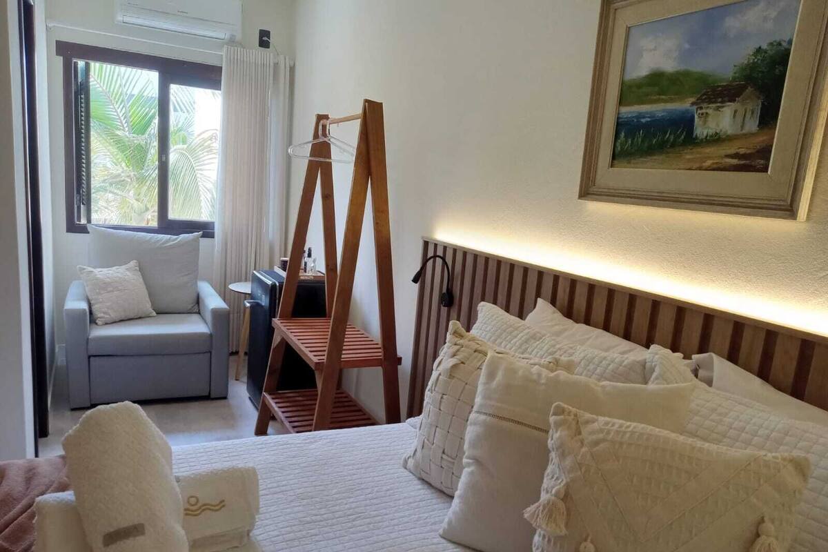 A hotel room with a bed, a sofa, a wooden hanger rack, and a painting on the wall.