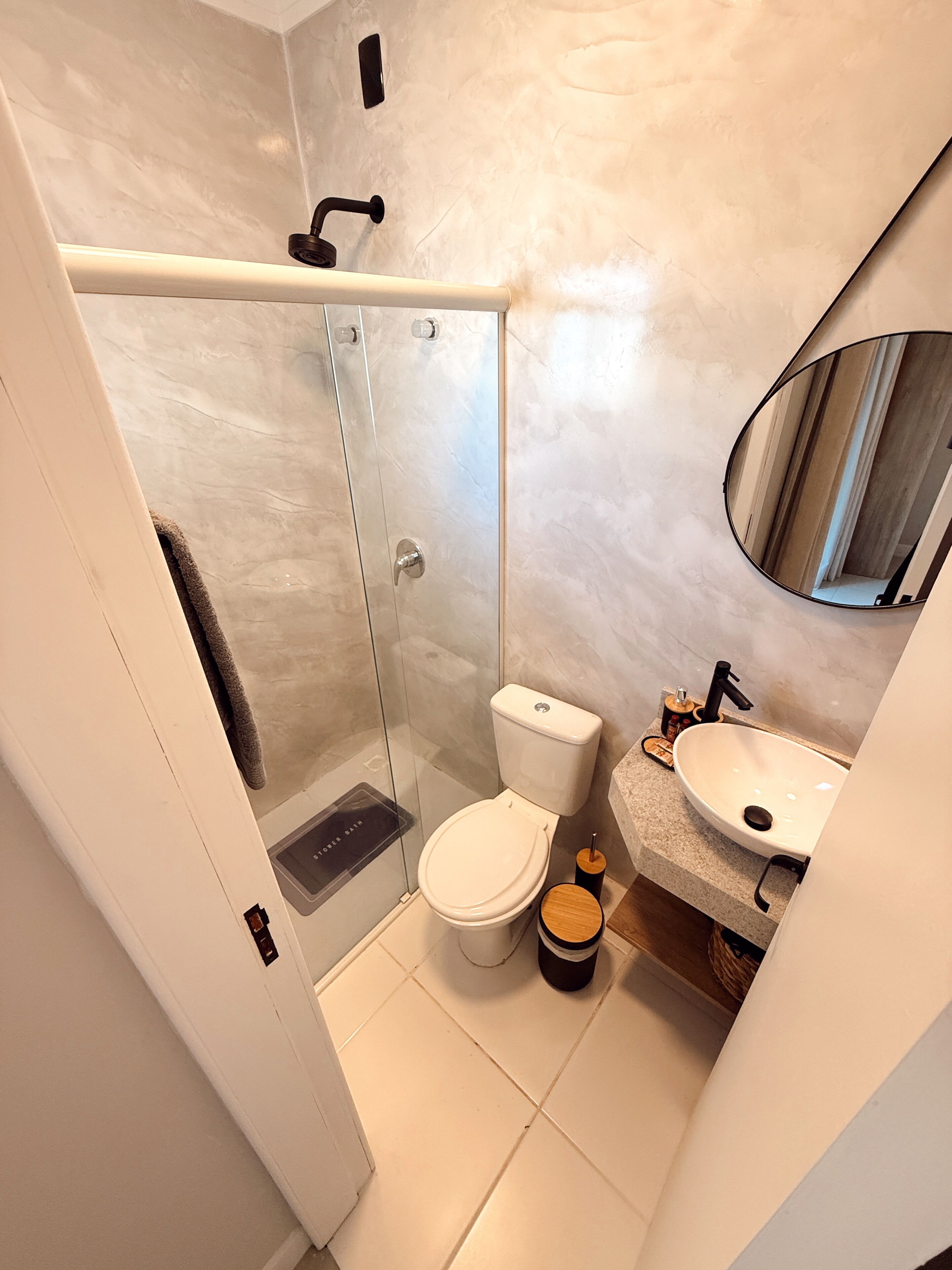 A modern bathroom with a glass-enclosed shower, a white toilet, and a sink with a mirror above it.
