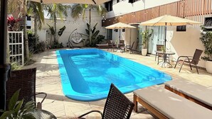 A swimming pool with lounge chairs and umbrellas, surrounded by a covered patio area. - Pousada Casa Californiana (Garopaba)