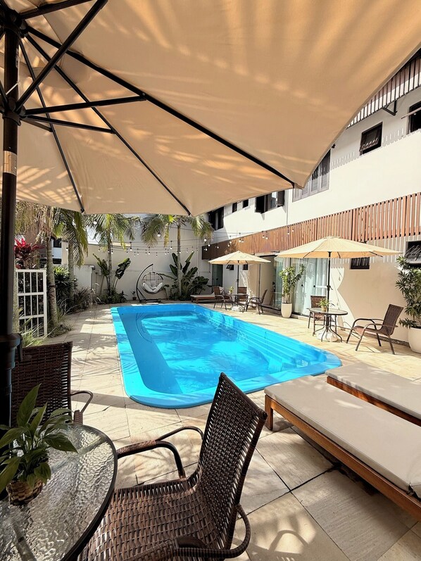 A swimming pool with lounge chairs and umbrellas, surrounded by a covered patio area. - Pousada Casa Californiana (Garopaba)