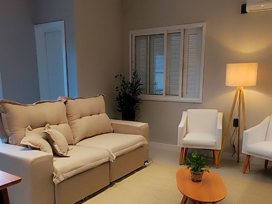 Una sala de estar moderna con un sofá color beige, una mesita de madera con una planta, sillones blancos y una lámpara.