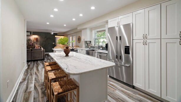 Una cocina moderna con armarios blancos, una isla de mármol y un refrigerador de acero inoxidable.
