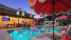 Zona de piscina con sillas de descanso, un flotador con forma de flamenco y una televisión mostrando un canal de Disney.