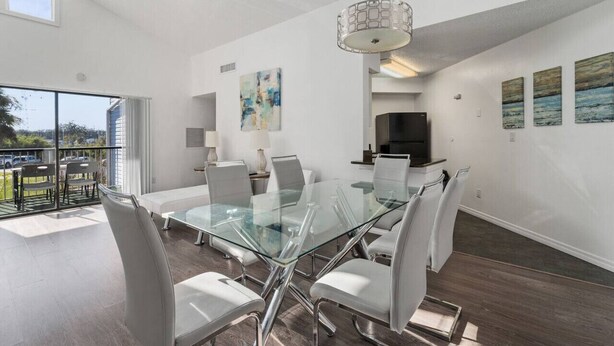 A modern dining area with a glass table and white chairs, a pendant light, and artwork on the walls. - Cozy Apt w/ Pool, Hot Tub, Golf, Near Downtown! (Orlando)