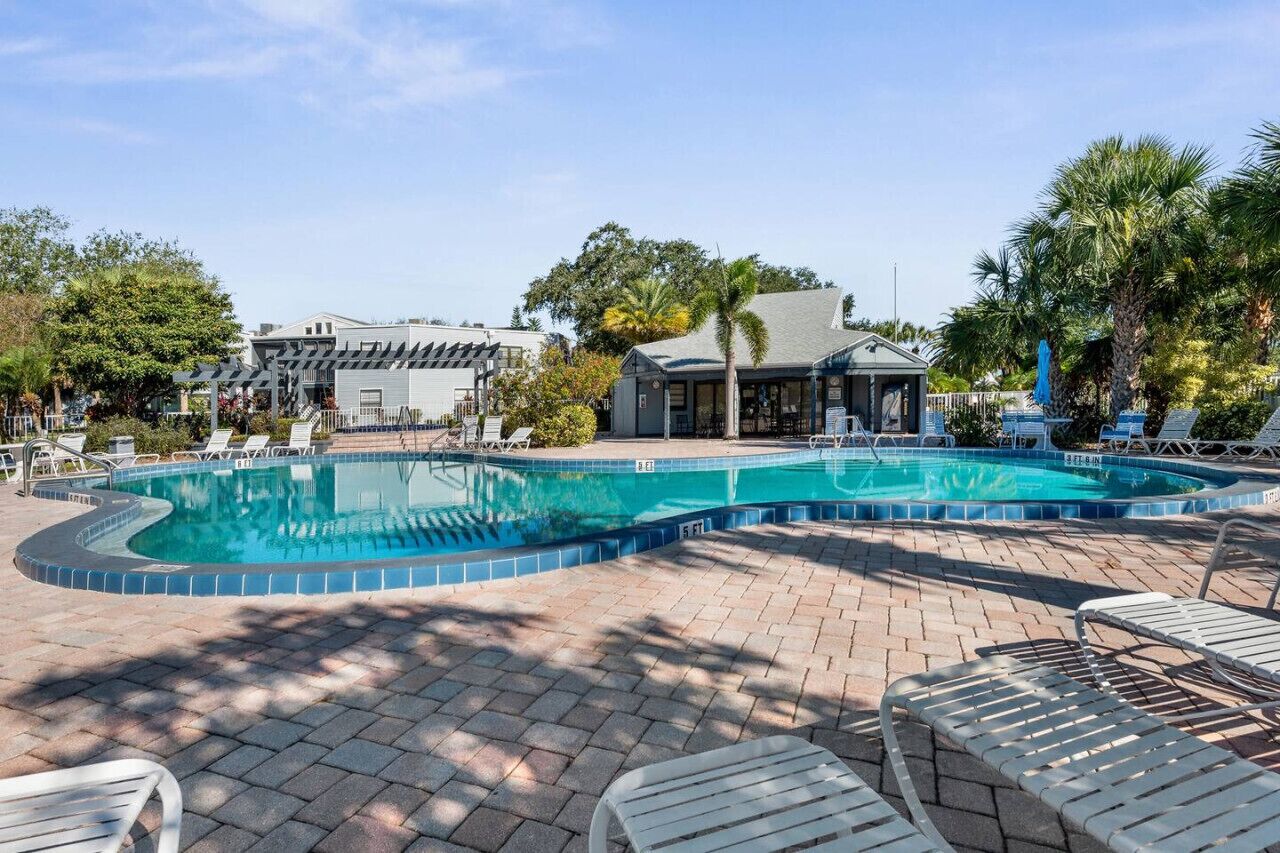 A swimming pool with lounge chairs, a covered seating area, and a building with a sloped roof.