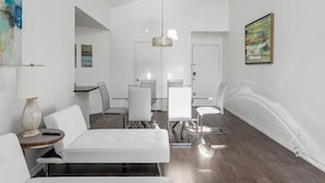 A modern, minimalist room with a white color scheme, featuring a dining table with chairs, a sofa, and a hanging light fixture. - Cozy Apt w/ Pool, Hot Tub, Golf, Near Downtown! (Orlando)