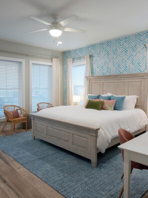 Une chambre à coucher avec un lit, deux fauteuils en osier, un ventilateur de plafond et un mur orné d’un motif en chevrons.