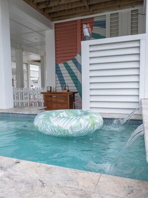 Un espace piscine agrémenté d’un matelas gonflable vert, d’une table en bois avec une carafe, et d’une statue de hibou décorative.