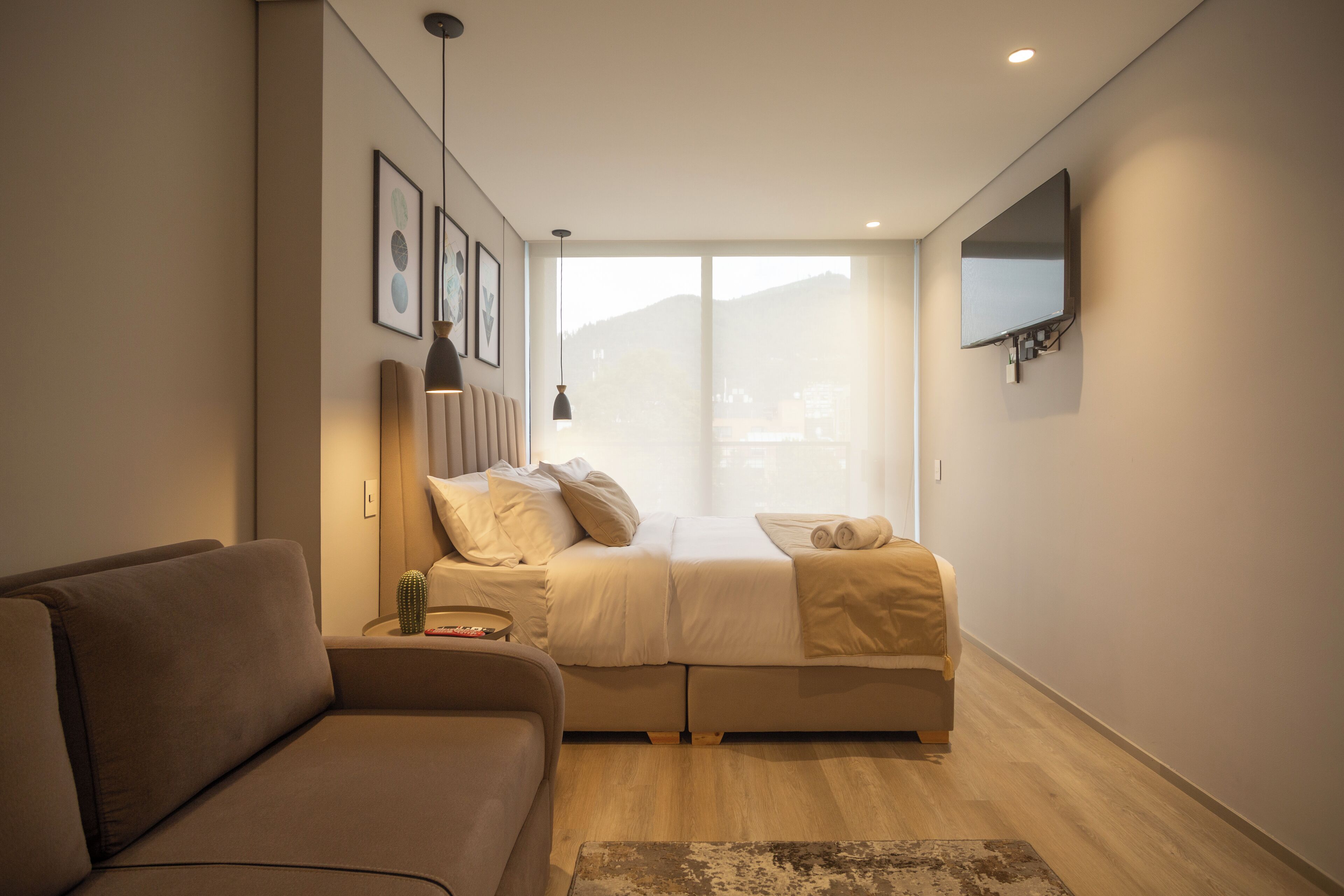 Un dormitorio moderno con un sofá, una cama con vistas y un televisor de pantalla plana montado en la pared.