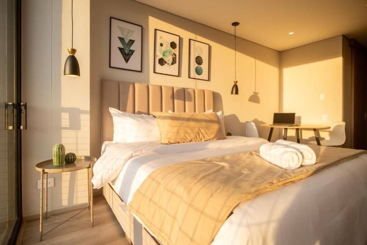 A hotel room with a large bed, a small table, a chair, and artwork on the wall.