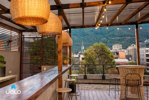 Une terrasse en bois avec des meubles en osier, un coin bar et une vue sur la ville et les montagnes.