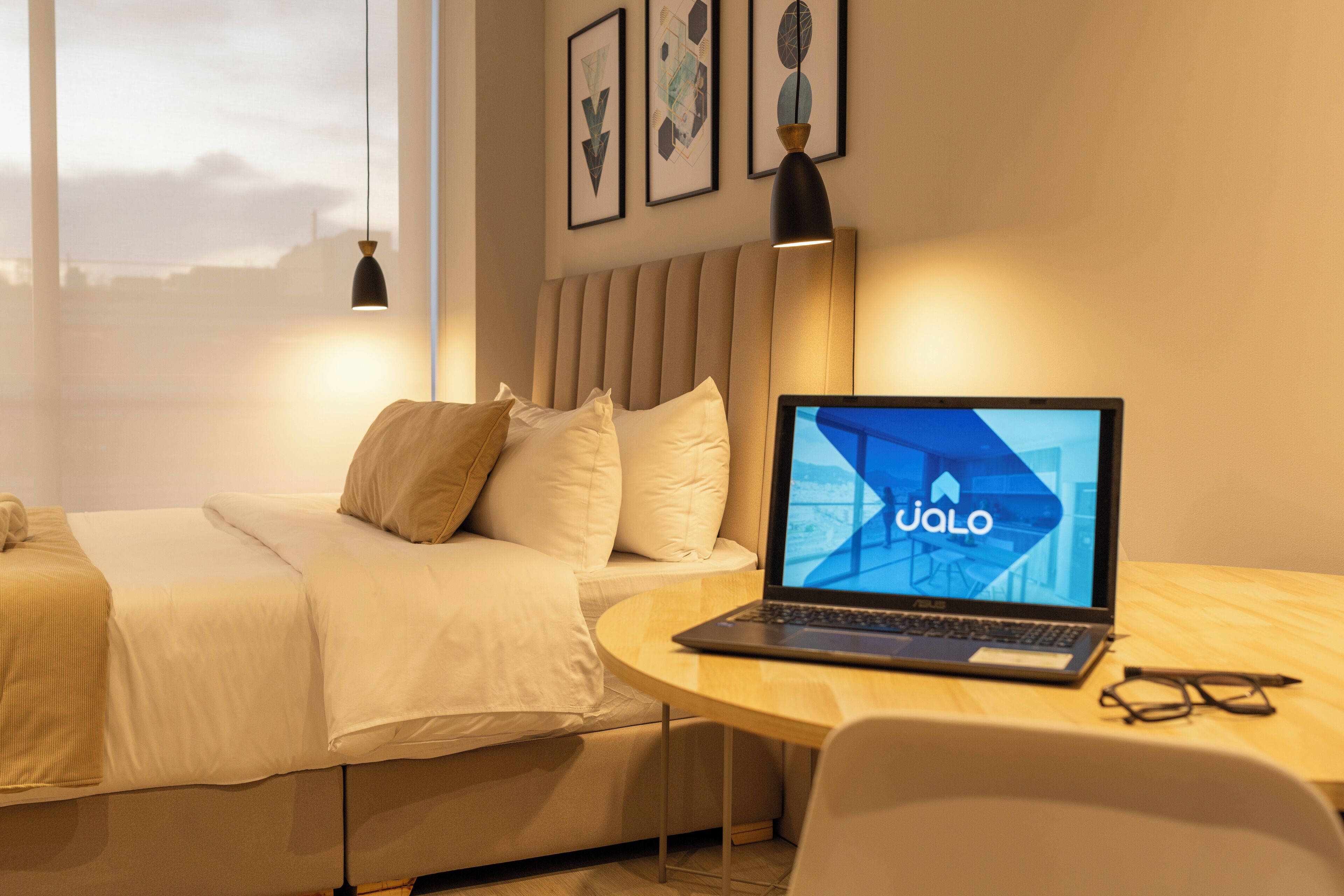 Habitación de hotel moderna con una cama, un escritorio con una computadora portátil y vistas a la ciudad.
