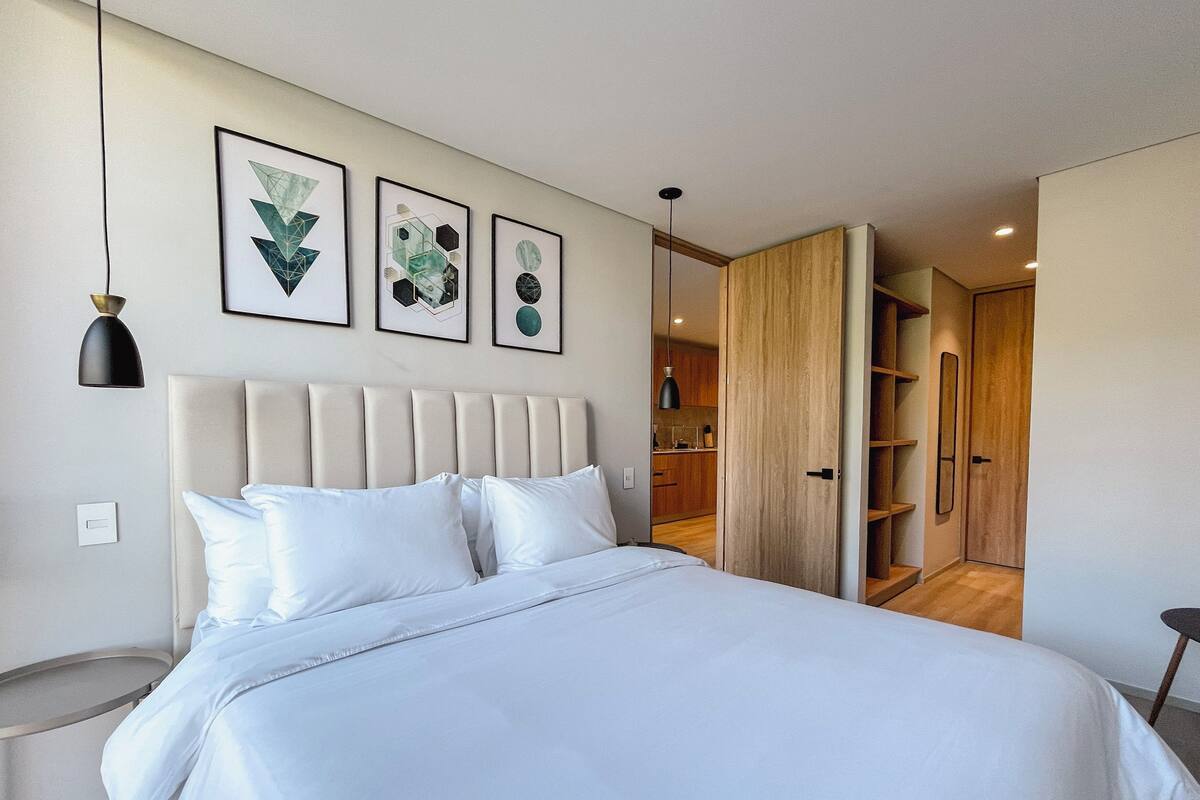 A modern bedroom with a large bed, a headboard, and three framed abstract artworks on the wall.