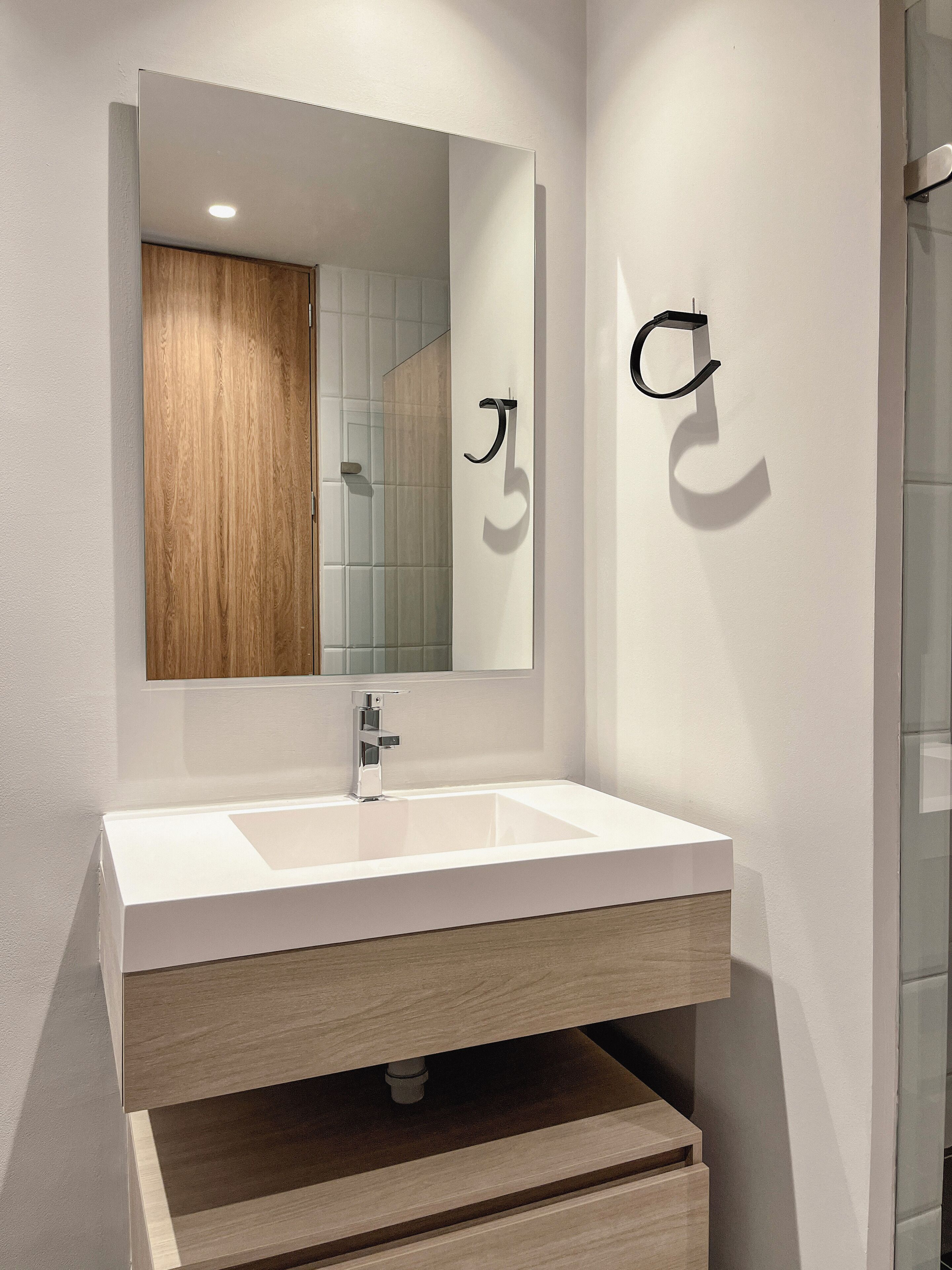 A modern bathroom with a white sink, wooden vanity, and a mirror reflecting a wooden door.