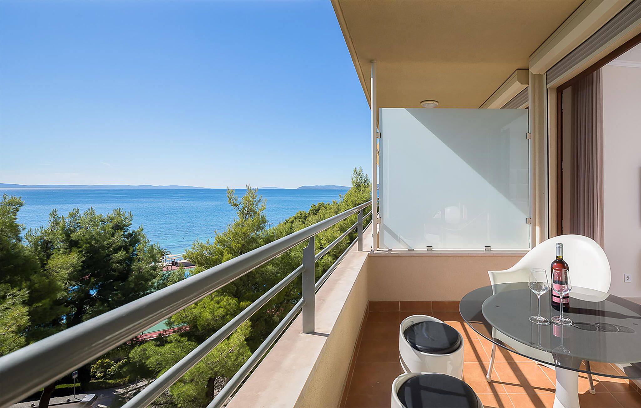 A balcony with a glass table, two chairs, and a bottle of wine.