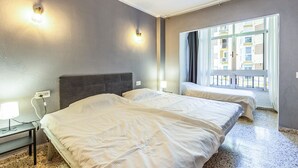 Et hotelværelse med to senge, et vindue der viser udsigt til bygninger, en vægmonteret lampe og en stikkontakt.