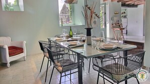 A dining area with a table set for four, surrounded by black chairs, a white cushioned chair, and a rustic ceiling. - De Rulinen - SAINT CLET (SAINT CLET)