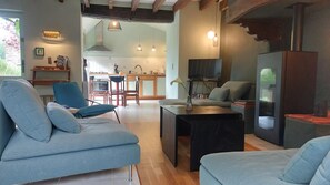 A living room with a sofa, a coffee table, and a TV. There is a kitchen in the background with a dining area.