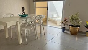 Een eetgedeelte met een witte tafel en stoelen, een decoratieve schaal en potplanten.