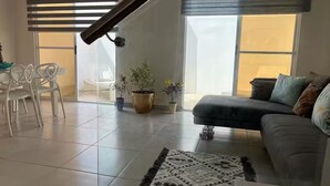 Een moderne woonkamer met een bank, een salontafel, een kamerkleed met patroon en potplanten.