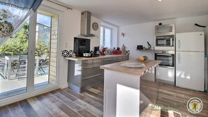 Una cocina moderna con una isla grande, horno empotrado, microondas y refrigerador. Hay una zona de comedor con mesa y sillas al lado de la cocina.