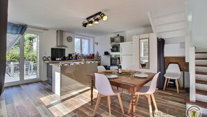 Una cocina amplia con una isla central, un comedor con una mesa de madera y sillas blancas, y una escalera que conduce a un piso superior.