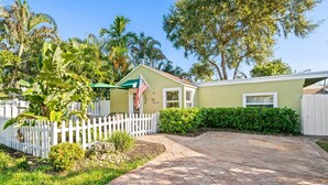 A house with a white picket fence, a paved driveway, and lush greenery including banana plants and palm trees. - Charming 2-bedroom house with WiFi and AC in welcoming Fort Lauderdale (Fort Lauderdale)