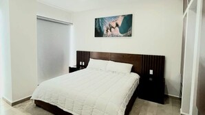 A modern bedroom with a large bed, a headboard with vertical lines, a wall-mounted artwork, and a sliding door closet. - Depa Bucearías playa (Bucerías)