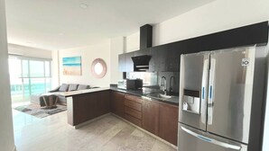 A modern kitchen with dark cabinetry, stainless steel appliances, and a large island. - Depa Bucearías playa (Bucerías)