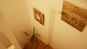 Un escalier en bois, avec une plante sur le côté gauche et deux panneaux en bois accrochés au mur, portant les inscriptions « Mer » et une étoile.
