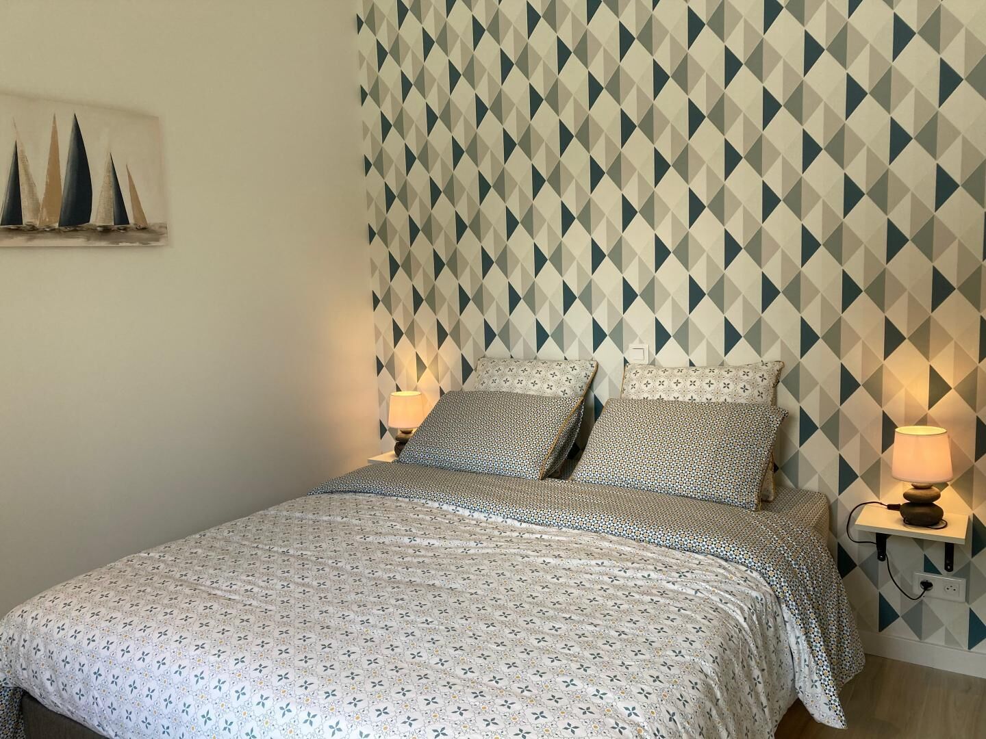 Un lit bien fait, avec une couvre-lit à motifs, deux oreillers et un mur orné d’un motif géométrique.