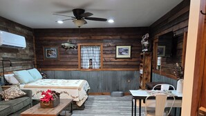 Une pièce confortable avec un lit, un bureau et une chaise. On y trouve un ventilateur de plafond, une fenêtre avec des rideaux et un climatiseur fixé au mur.