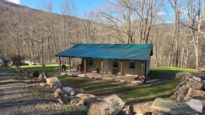 Une cabane rustique avec un toit végétalisé, entourée d’un paysage naturel composé de grands rochers et d’arbres.