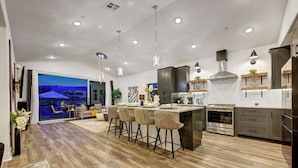 A modern kitchen with a central island, bar stools, and a dining area with a view of the outdoors.