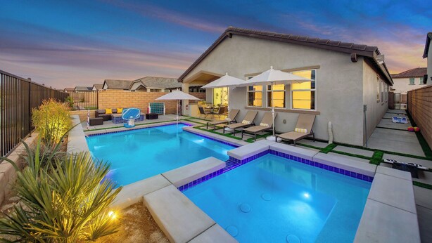 A swimming pool with lounge chairs and umbrellas, surrounded by a house and a fence.