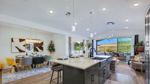 A modern kitchen with a large island, dining area with yellow chairs, and a living room with a view of a golf course.