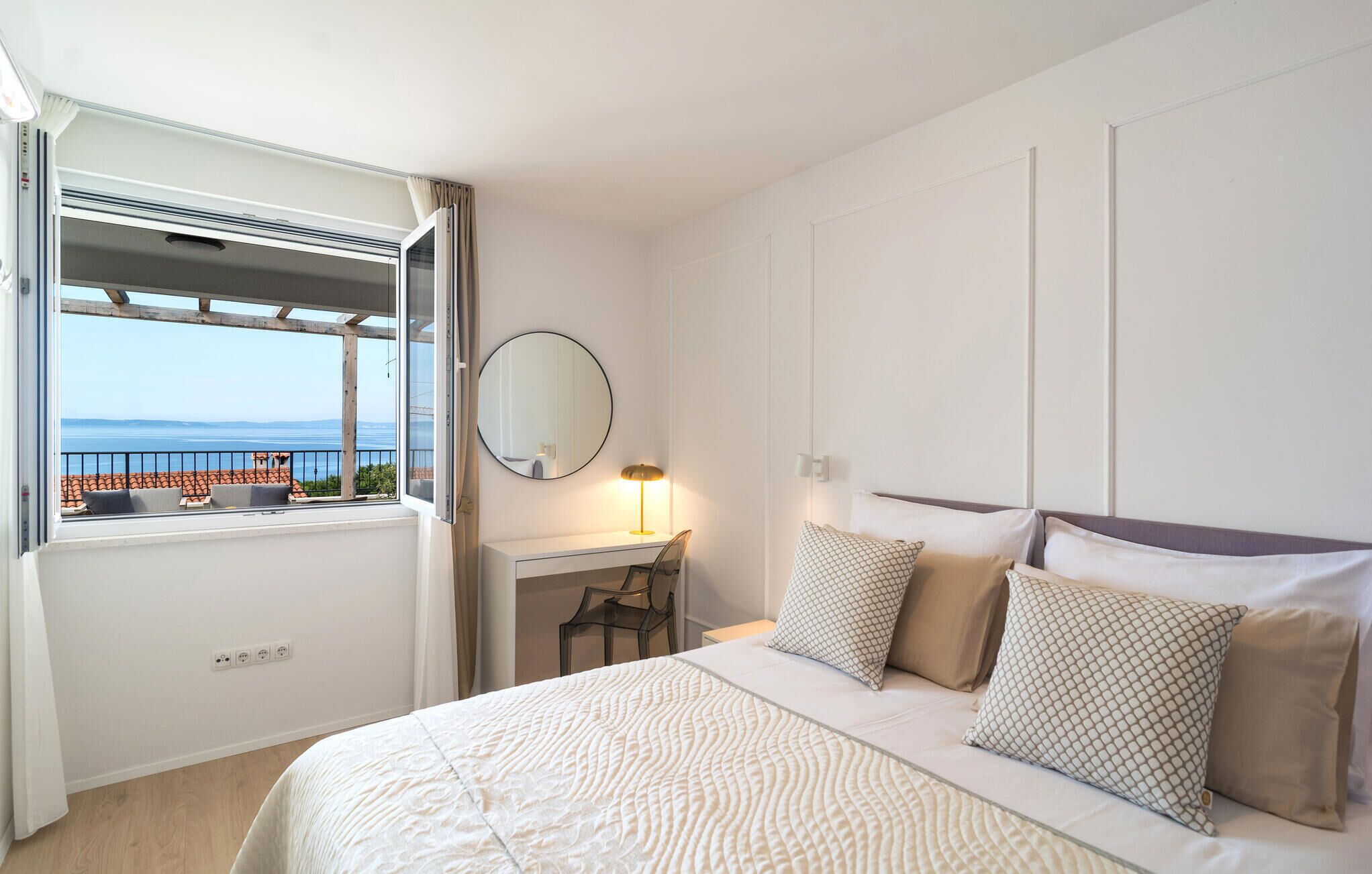 Habitación de hotel con cama, escritorio, silla, lámpara y vista al mar a través de una ventana.