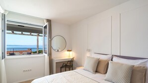 A hotel room with a bed, a desk, a chair, a lamp, and a view of the sea through a window. - Lovely apartment in Podstrana with WiFi (Podstrana)