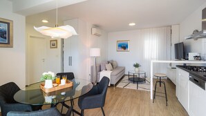 A modern kitchen with a stove, oven, and microwave. There is a dining area with a glass table and chairs, a sofa, and a small round table with a plant. - Lovely apartment in Podstrana with WiFi (Podstrana)