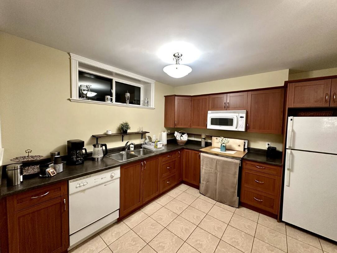 A kitchen with wooden cabinets, a microwave, a dishwasher, and a window above the sink.