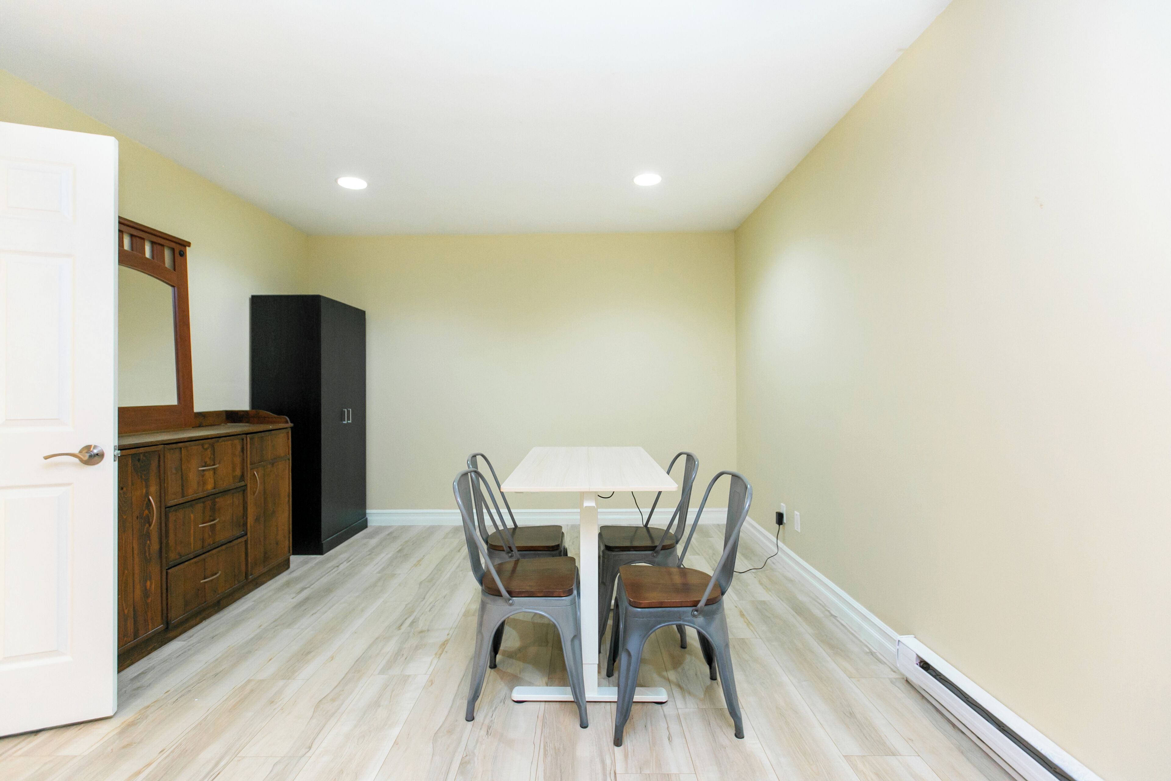 Un coin repas avec une table blanche et quatre chaises, un buffet en bois et un réfrigérateur noir.