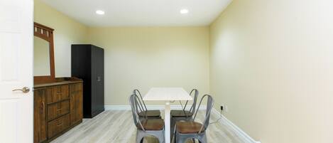 Un coin repas avec une table blanche et quatre chaises, un buffet en bois et un réfrigérateur noir.