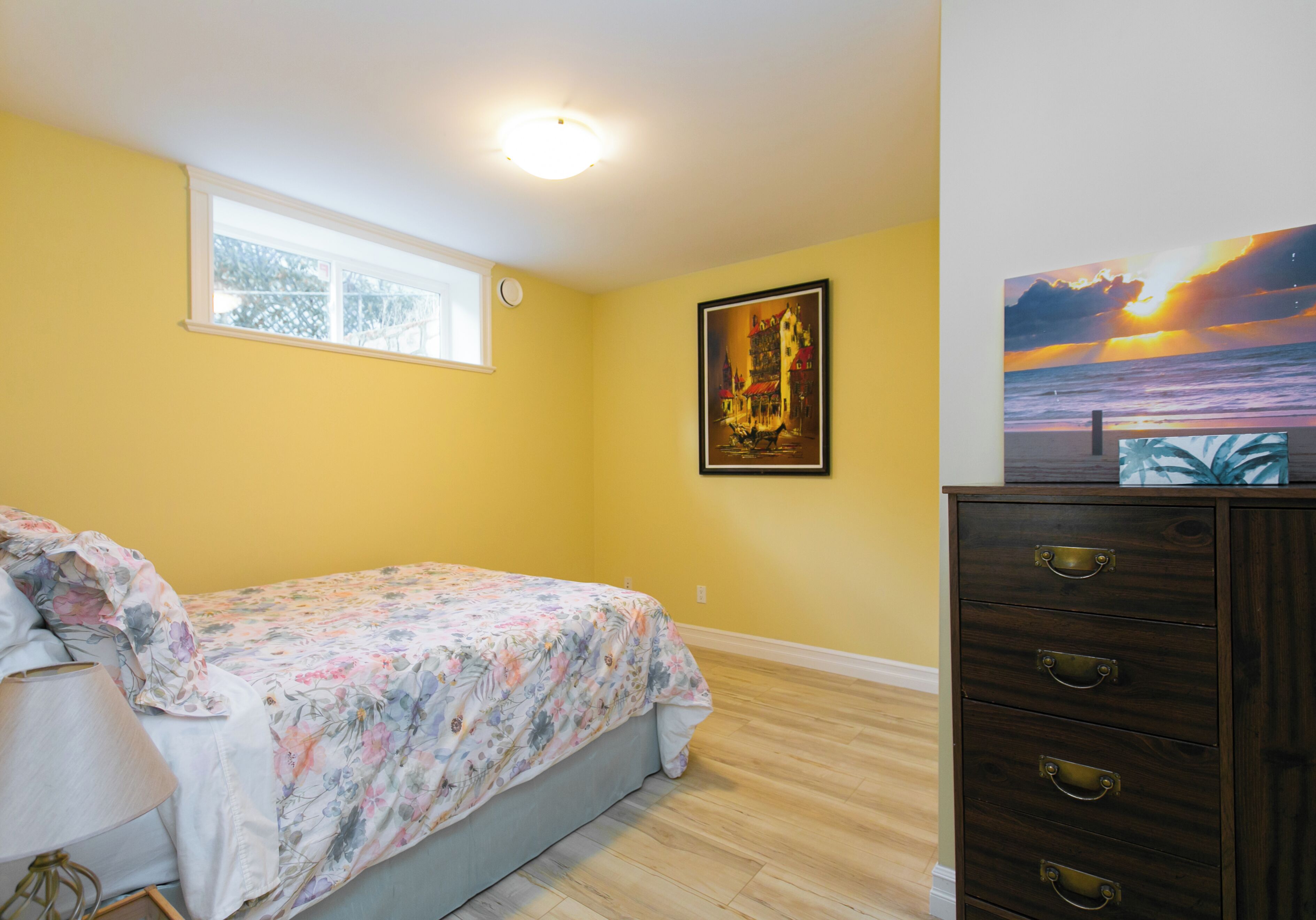 A bedroom with a bed, a dresser, a window, and two wall art pieces.